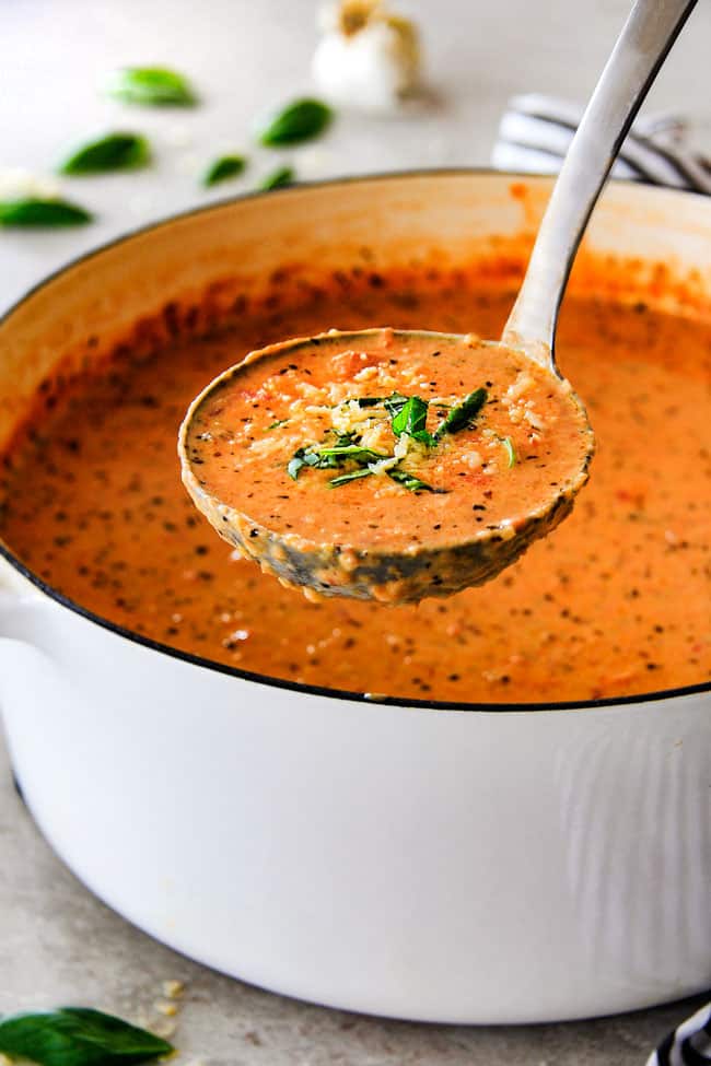 This Tomato Basil Soup recipe is our family favorite!ย Its super easy without any chopping! bursting with flavor and I love the addition of Parmesan!ย ย serving creamy tomato basil soup with a silver ladle.