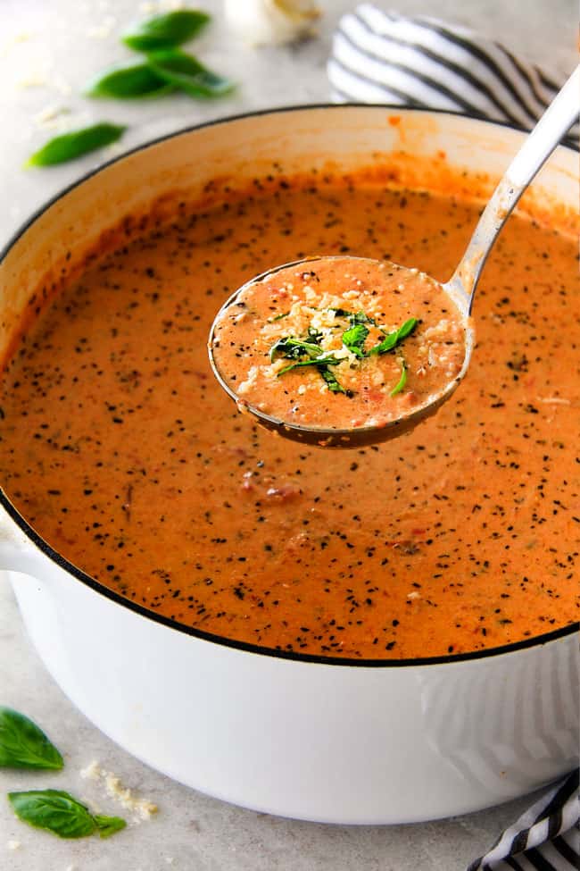 This Tomato Basil Soup recipe is our family favorite!ย Its super easy without any chopping! bursting with flavor and I love the addition of Parmesan!ย ย a ladle of Creamy Tomato Basil Soup raised above a big soup pot.