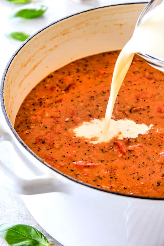 This Tomato Basil Soup recipe is our family favorite!ย Its super easy without any chopping! bursting with flavor and I love the addition of Parmesan!ย ย showing how to make tomato basil soup by adding cream to a large pot of tomato soup