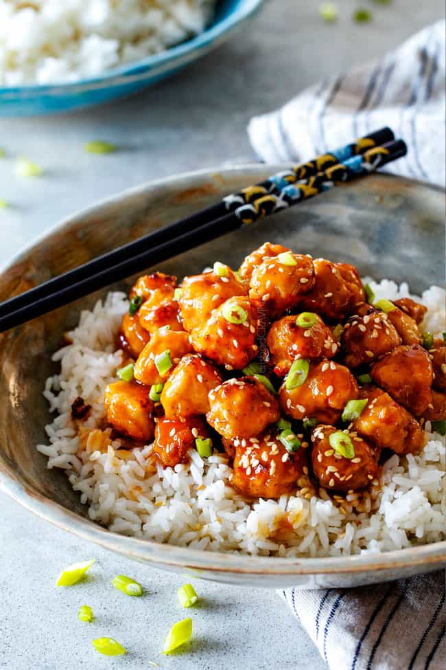 General Tso's Chicken over white rice with black chopsticks.
