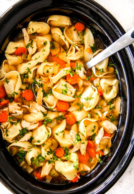 cheese tortellini, carrots, celery, onions, garlic and spices in crockpot with soup ladle for This is the BEST Slow Cooker Chicken Tortellini Soup you will ever try!  It's super easy, seasoned to perfection and a comforting, satisfying dinner any night of the week!  