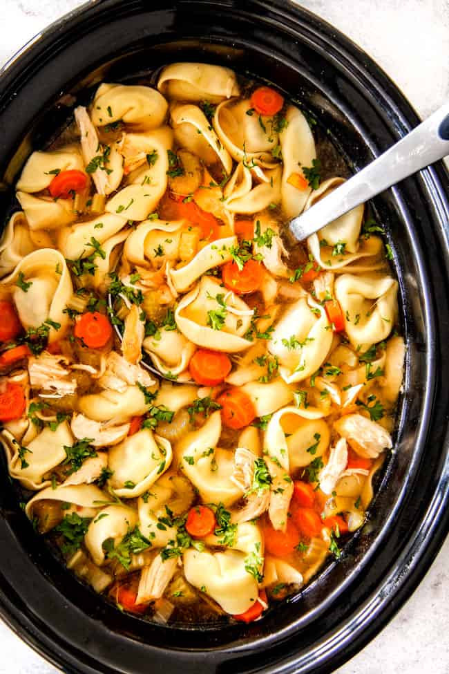 This is the BEST Slow Cooker Chicken Tortellini Soup you will ever try!ย It's super easy, seasoned to perfection and a comforting, satisfying dinner any night of the week!ย ย top view of Chicken Tortellini Soup with cheese tortellini, carrots, celery, onions, garlic and spices in pot