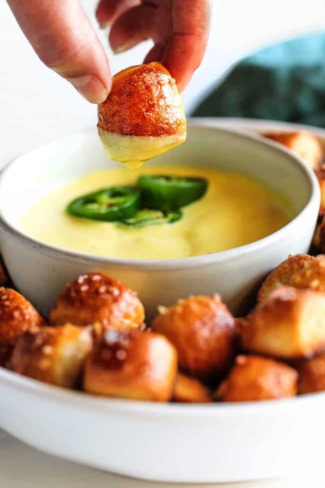 a hand holding onto a pretzel bite covered in cheese sauce