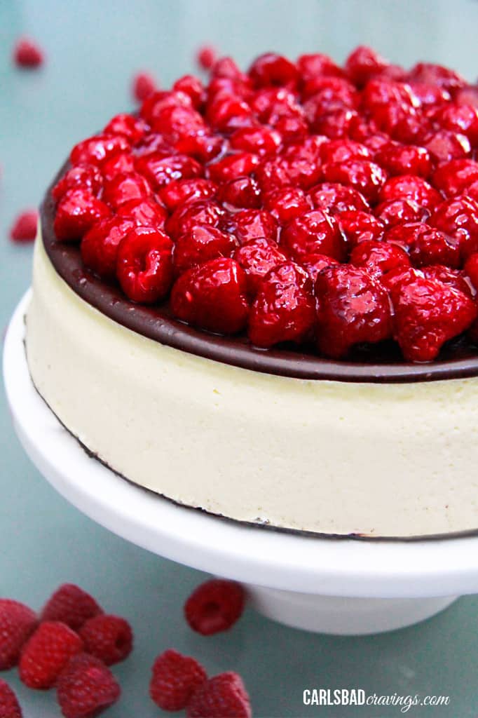 Chocolate Raspberry Cheesecake on a white pedestal with fresh raspberries on top