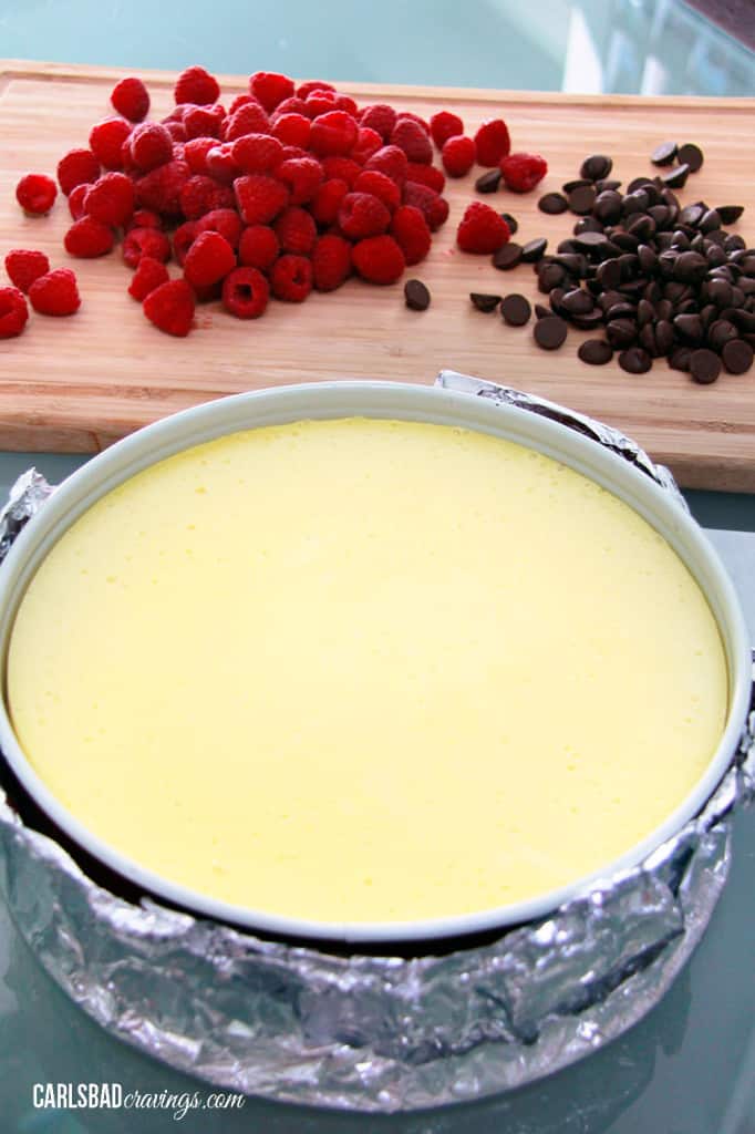 plain baked cheesecake in a pan waiting to be topped with raspberries 