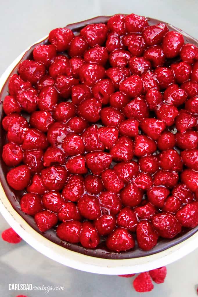 Chocolate Raspberry Cheesecake on a white pedestal with fresh raspberries on top