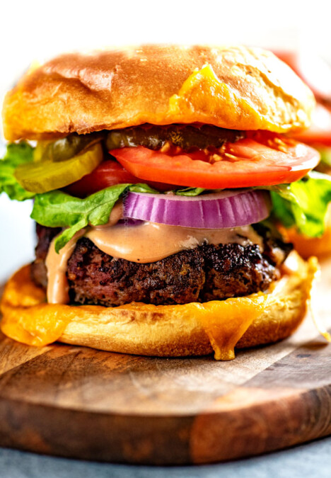 up close of ultimate burger recipe piled with cheese, bacon, tomatoes and lettuce