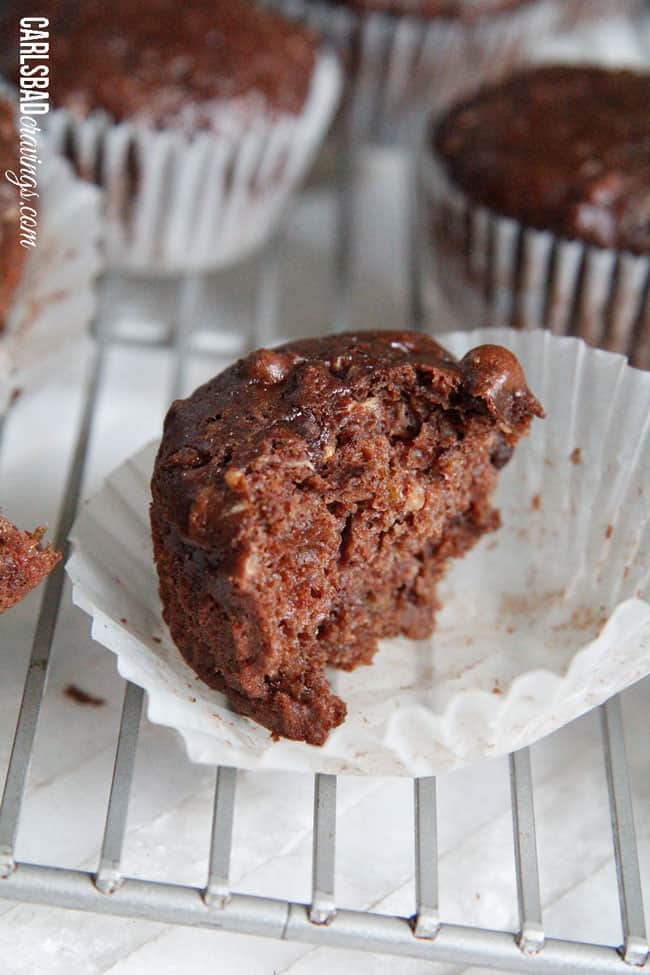 Chocolate Zucchini Muffins with DOUBLE the CHOCOLATE, ZERO added fat and a whole lot of yum!! This Chocolate Zucchini Muffins Recipe is baked with applesauce and vanilla yogurt that are crazy moist and chocolaty!ย You will devour these by the handfuls - becauseย you can! a half eaten moist chocolate zucchini muffin in a white wrapper