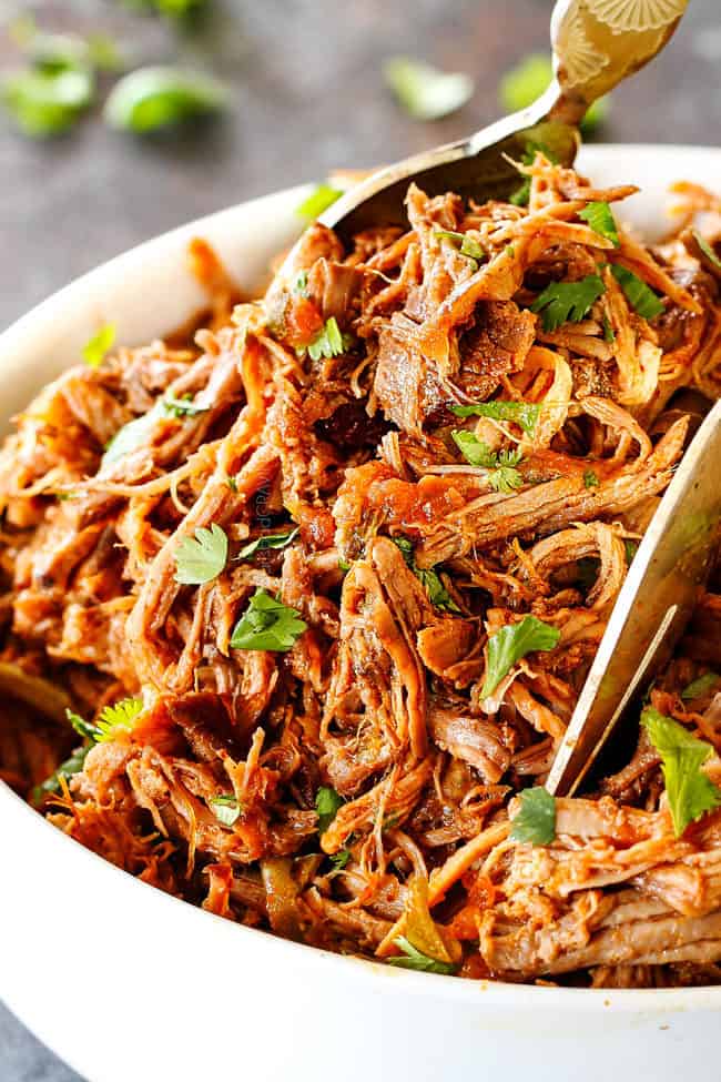 up close of Best Cafe Rio Sweet Pork in a white bowl with gold tongs picking up pork