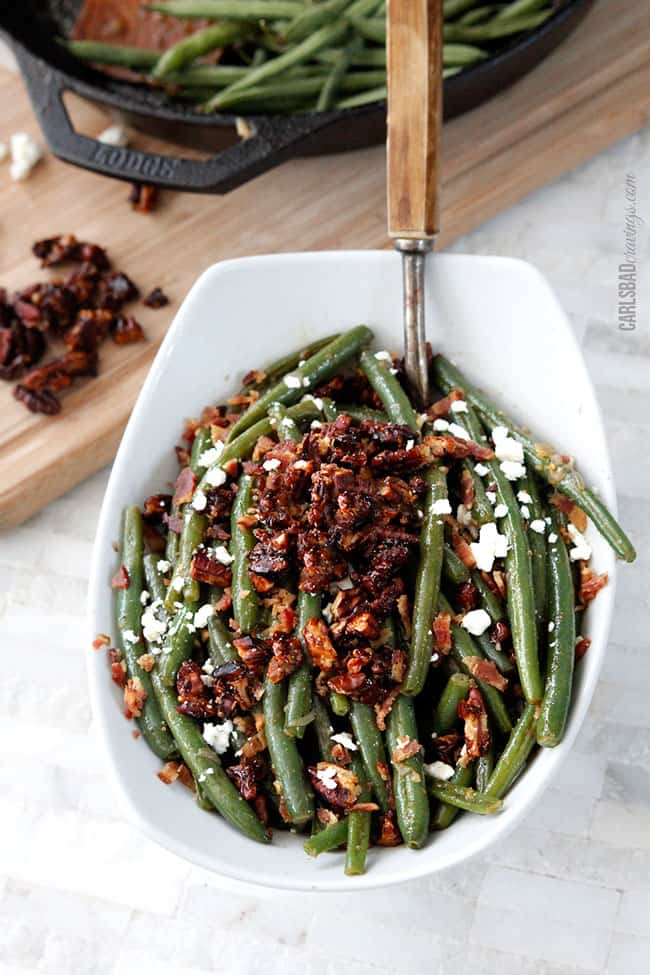 front view of green beans recipe with bacon and pecans with a wood serving spoon