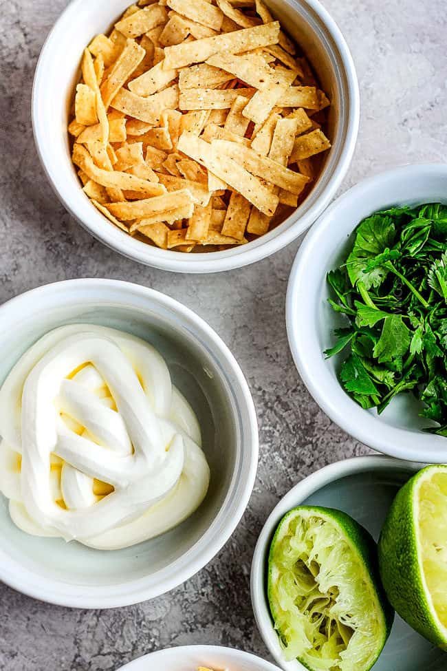 top view showing toppings for crockpot chicken tortilla soup of sour cream, cilantro, limes and cheese