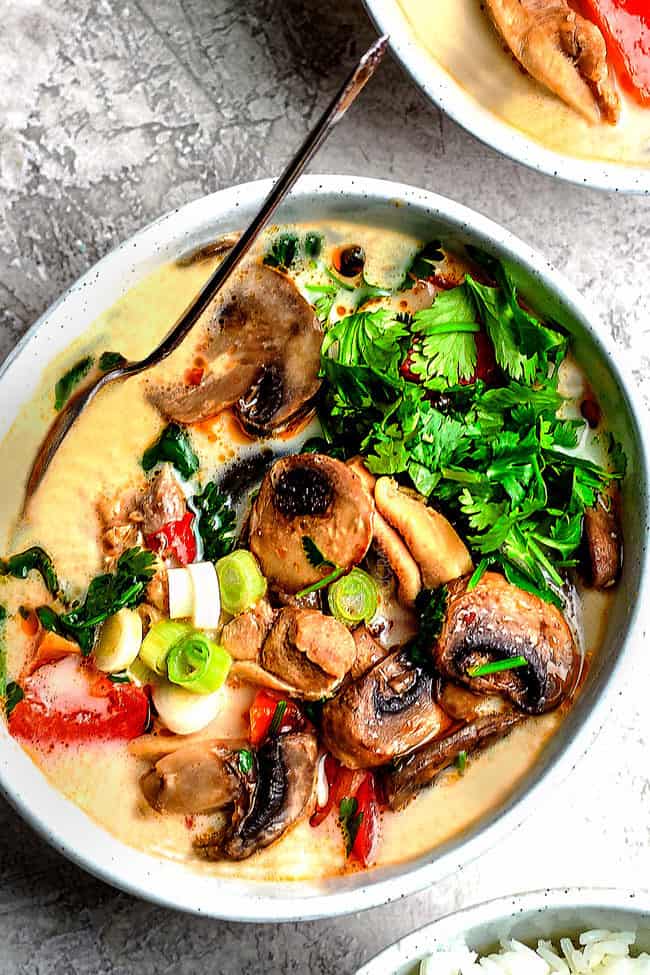 a bowl of tom kha gai soup with mushrooms, bell peppers and green onions