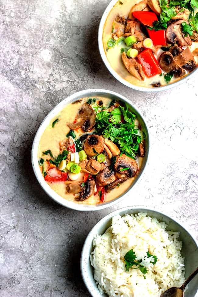Top view of a bowl of gluten free Tom Kha Gai with a bowl of rice and cilantro garnishes