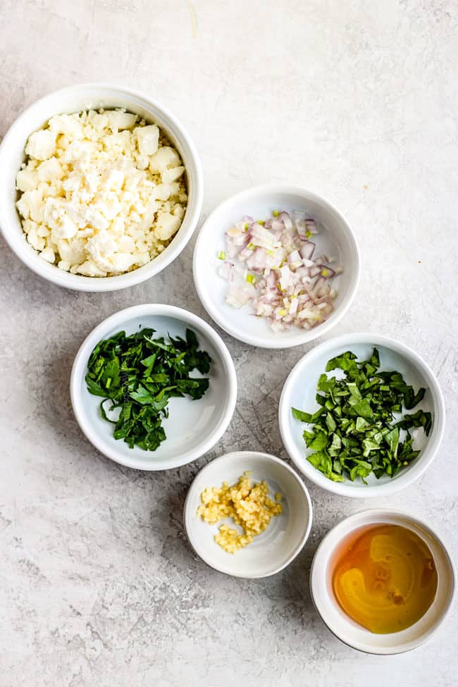 showing how to to make spicy whipped feta dip by lining up feta, cream cheese, garlic, red onions, herbs