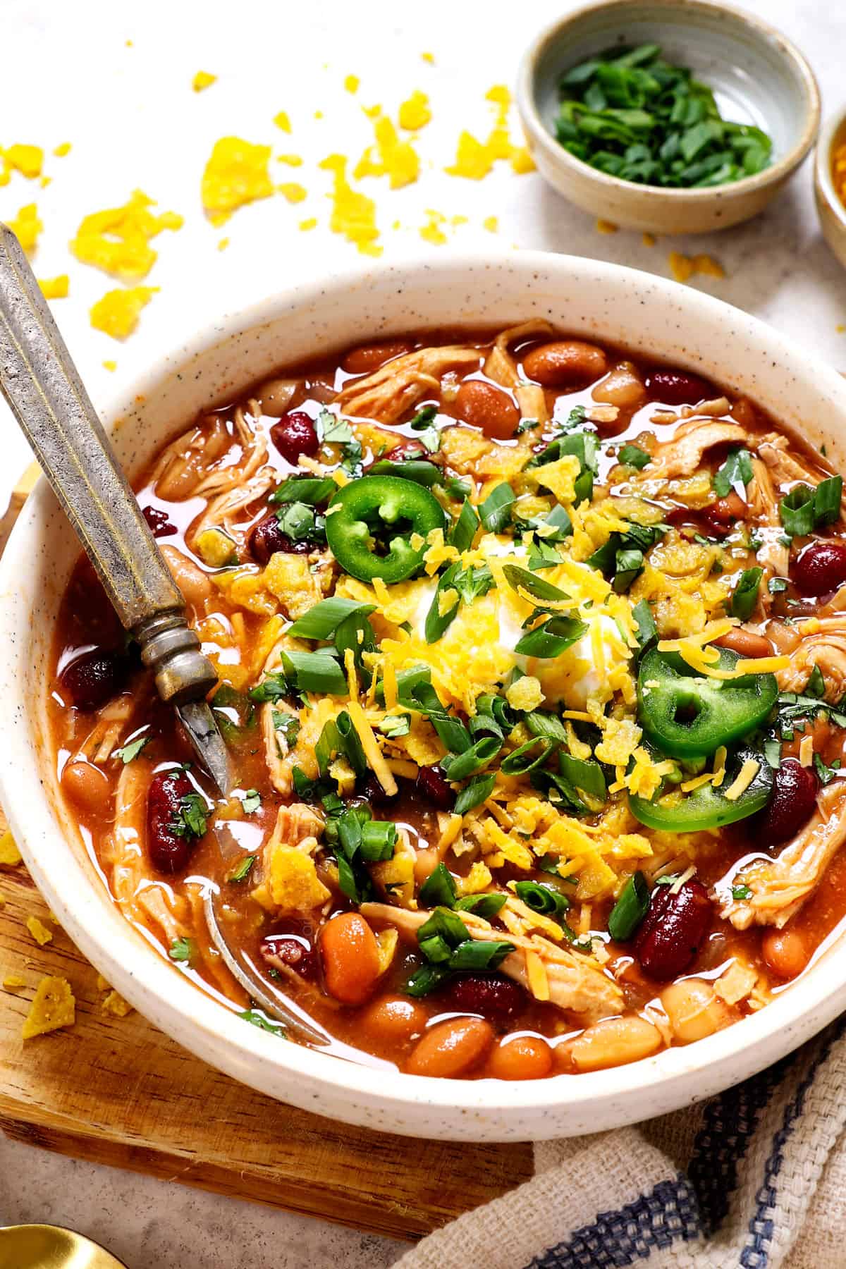 showing how to serve chicken chili by adding cheese, sour cream, green onions and tortilla chips