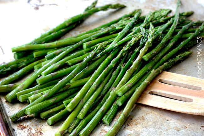 roasted asparagus on baking sheet being scooped up with a spatula