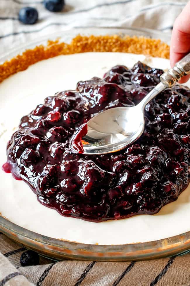 10 Minutes to the BEST Blueberry Sauce or Syrup ever! Amazing on cheesecake, pancakes, crepes, French Toast, etc. and SO EASY! smoothing fresh blueberry sauce over cheesecake with the back of a spoon