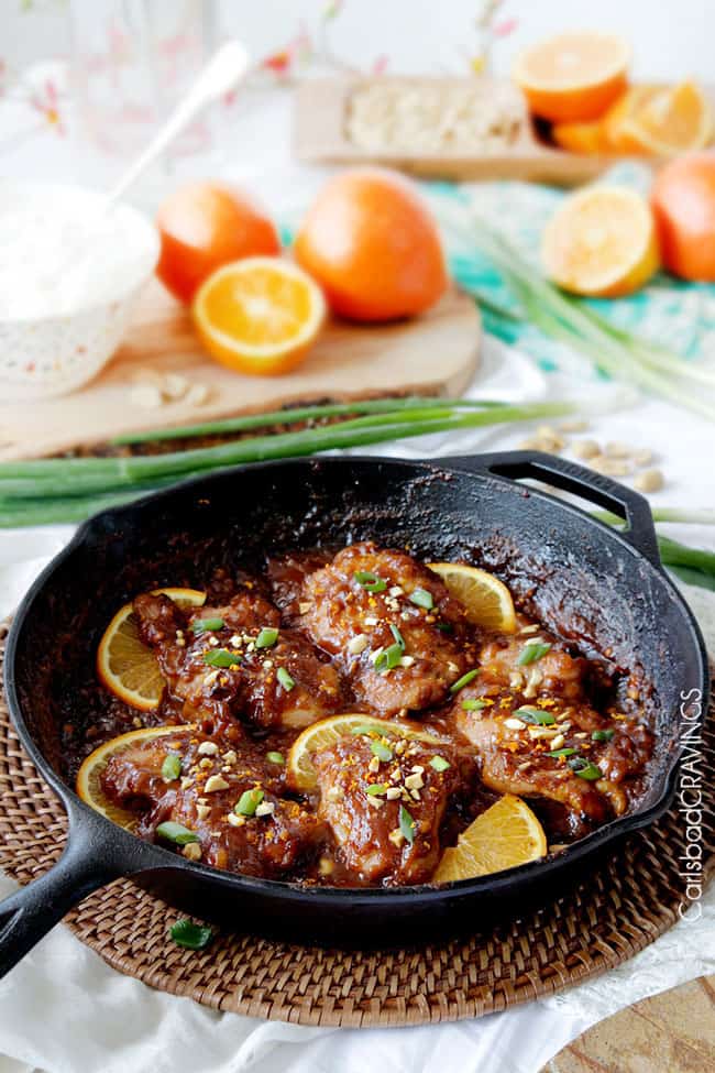 Close up of Sticky Thai Peanut Orange Chicken with nuts and chive garnish in a black skillet.