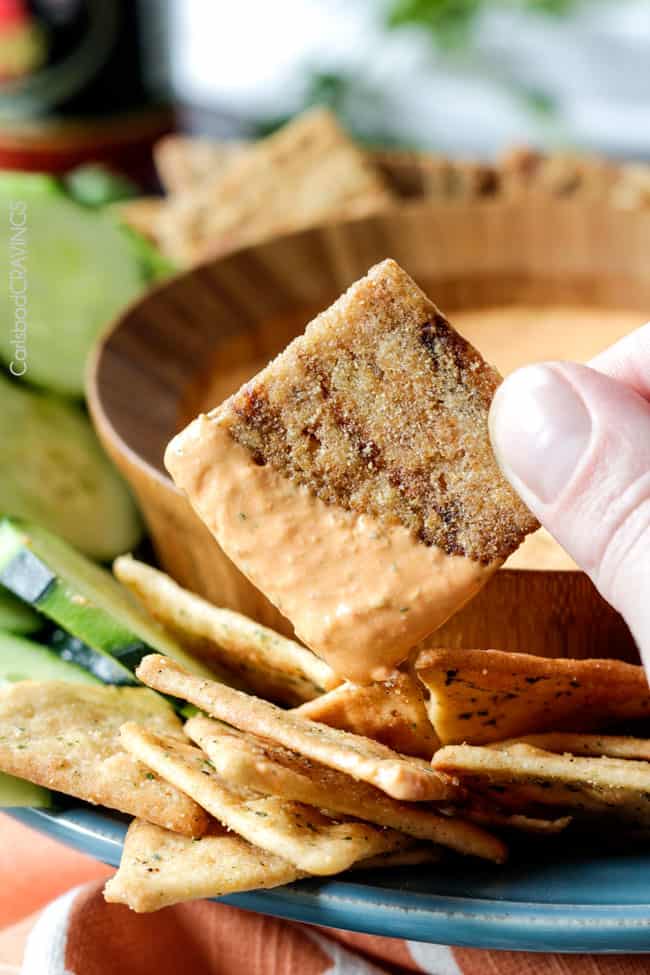 A cracker dipped in a bowl of Roasted Red Pepper Feta Dip.