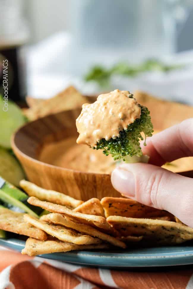 Broccoli held up with dip of Roasted Red Pepper Feta Dip.