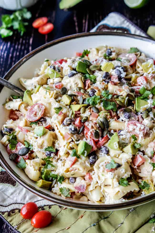 Make ahead, favorite potluck Southwest Pepper Jack Tortellini Salad = cheesy pillows of tortellini, sweet corn, black beans, avocado, bell peppers, etc. bathed in Creamy Salsa Dressing and garnished with bacon, Pepper Jack, sunflower seeds. Oh my YUM! #tortellini #pastasalad #southwest #salad