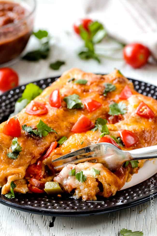 Easy, hearty Breakfast Enchiladas stuffed with your favorite breakfast ingredients then smothered with intoxicatingly delicious Creamy Salsa Sauce! These enchiladas are totally customizable, perfect for your leftover holiday ham AND you can assemble the night before and bake the next day! a fork biting into cheesy breakfast enchiladas on a plate