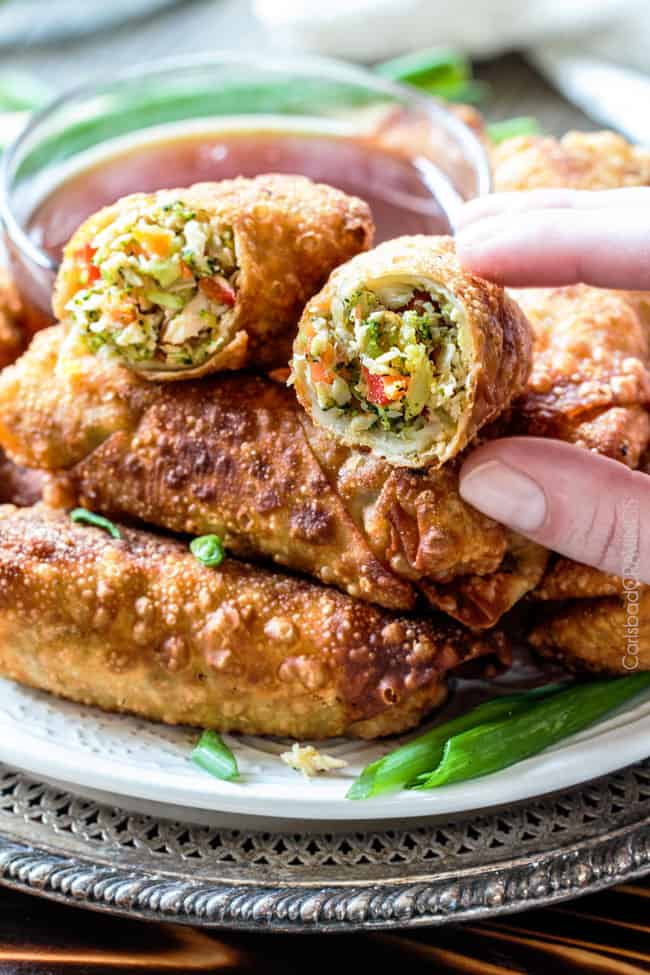 Sweet and Sour Chicken Egg are the best egg rolls Iโve ever had with the best sweet and sour sauce! And made extra fast with the food processor. I am bringing these to all my holiday parties! #appetizer #NewYears #Christmas up close of a hand picking up a Chinese chicken egg roll