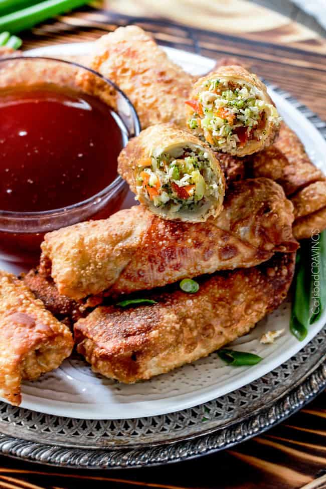 Sweet and Sour Chicken Egg are the best egg rolls Iโve ever had with the best sweet and sour sauce! And made extra fast with the food processor. I am bringing these to all my holiday parties! #appetizer #NewYears #Christmas a pile of homemade chicken egg rolls on a plate with one cut open with the chicken filling spilling outt