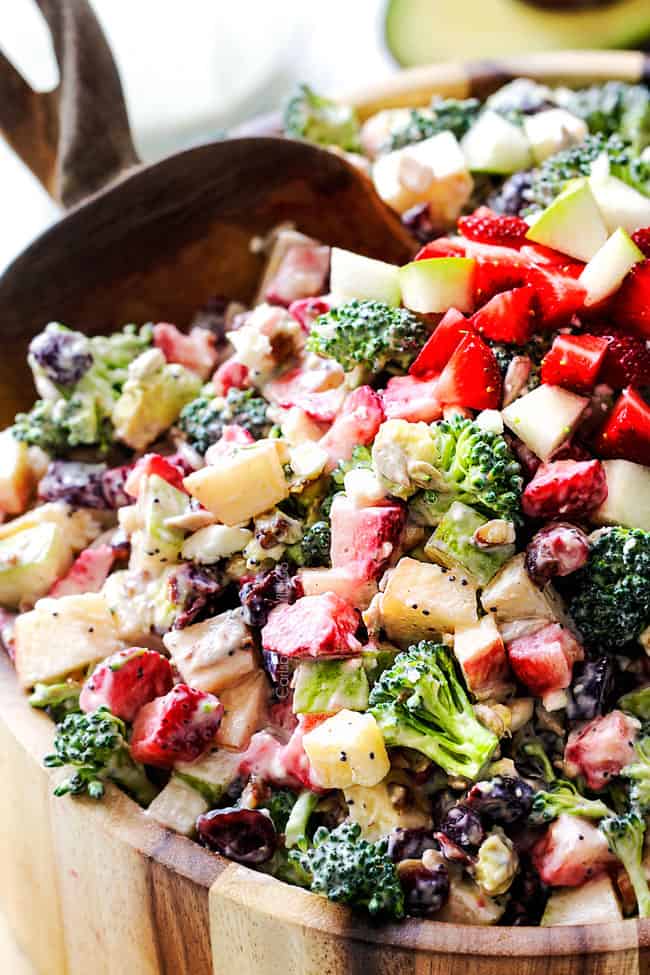 up close of broccoli tossed with creamy dressing with mayonnaise in a wood bowl being scooped by a wood spoon