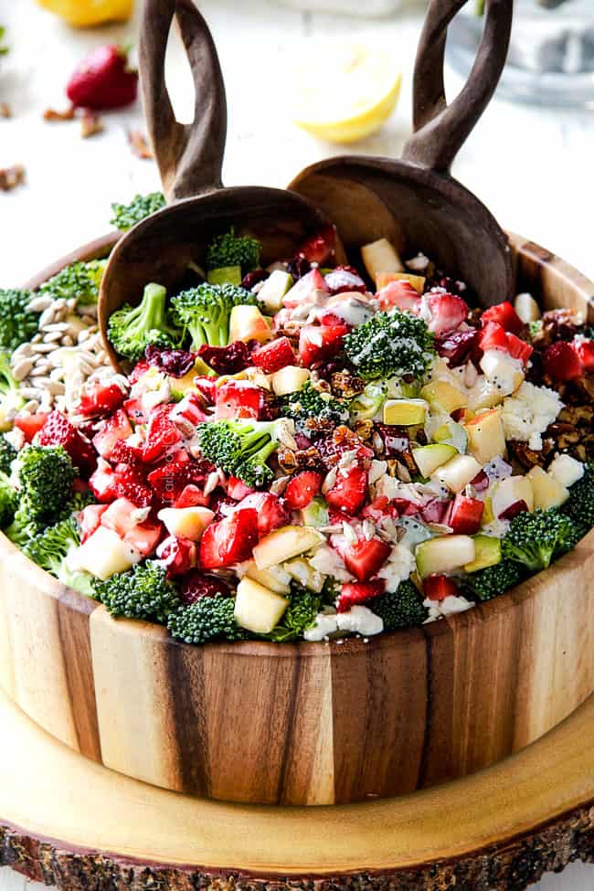 combining best broccoli salad in a wood bowl with wood tongs with creamy dressing