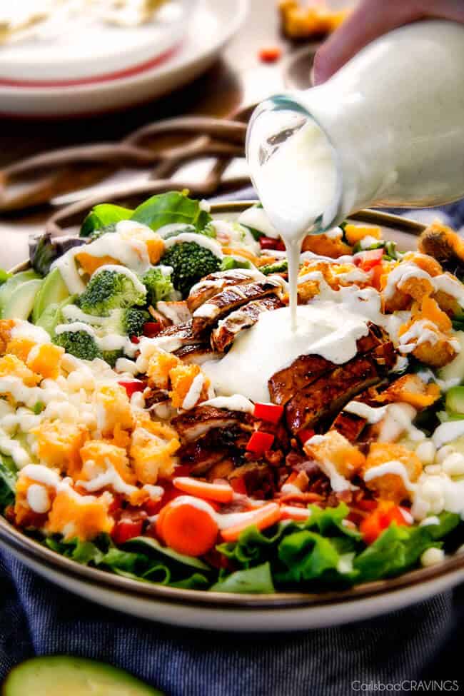 Chicken Bacon Ranch Salad with dressing being poured on top with cheese and croutons.