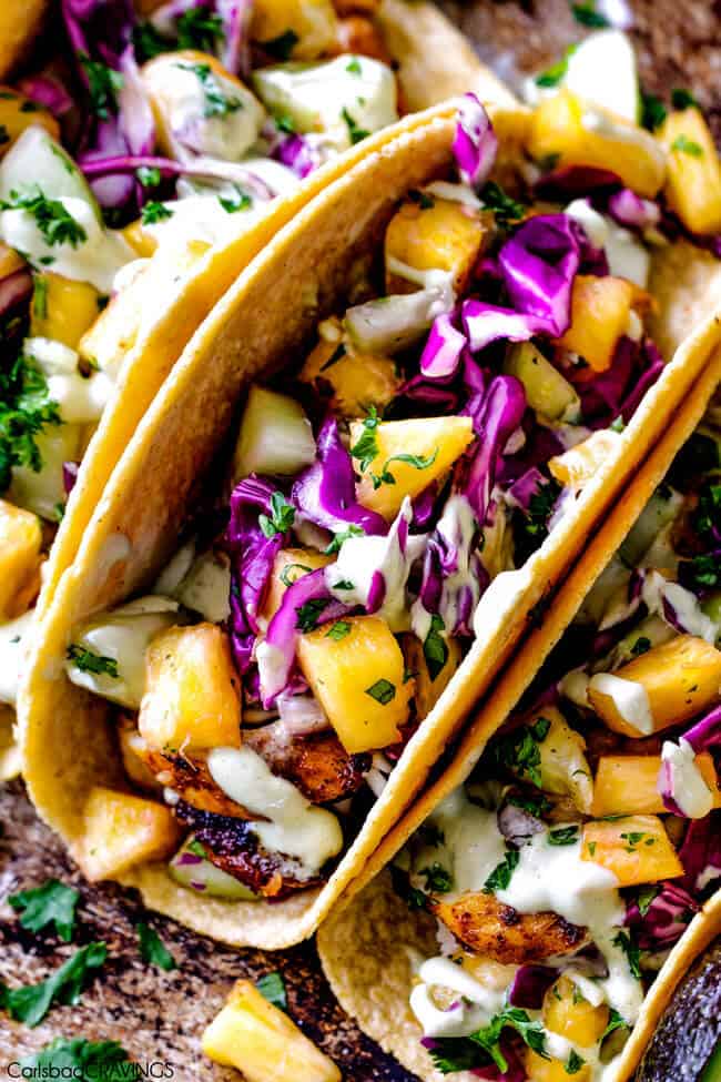 Mind blowing Blackened Tilapia Fish Tacos with a quick marinade and the most flavorful spice rub! These are hands down the BEST FISH TACOS ever! And the sweet and tangy Pineapple Cucumber Slaw and Avocado Crema hit this one out of the park! seriously better than my favorite restaurant! a line of tilapia fish tacos in corn tortillas with cabbage and fish sauce