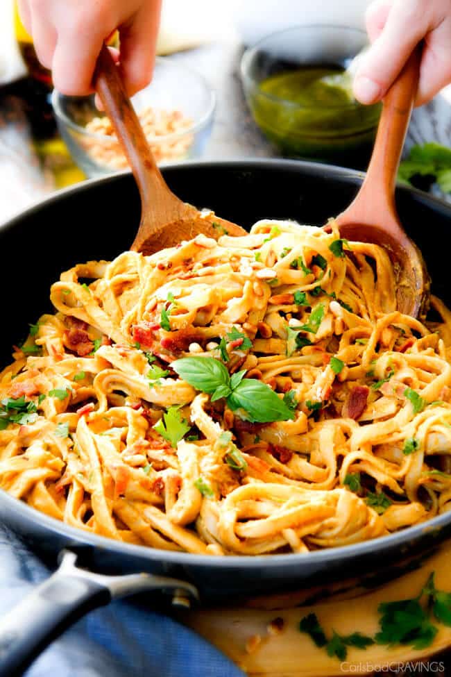 Creamy Butternut Squash Pasta - silky quick and easy pasta that is SO creamy and absolutely addicting! Infused with fresh Parmesan, seasoned to perfection and topped with crispy bacon and toasted pine nuts! #glutenfree #fall two wooden tongs scooping up easy Butternut Squash Pasta with sage in a skillet