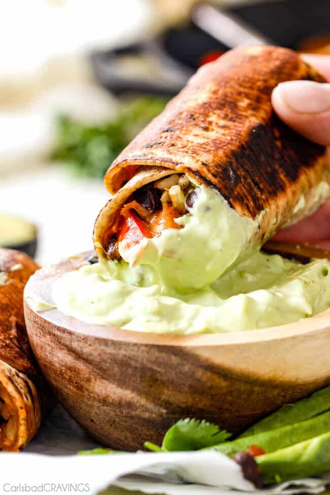 Close up of Chicken Fajita Wraps being dipped in avocado cream sauce.