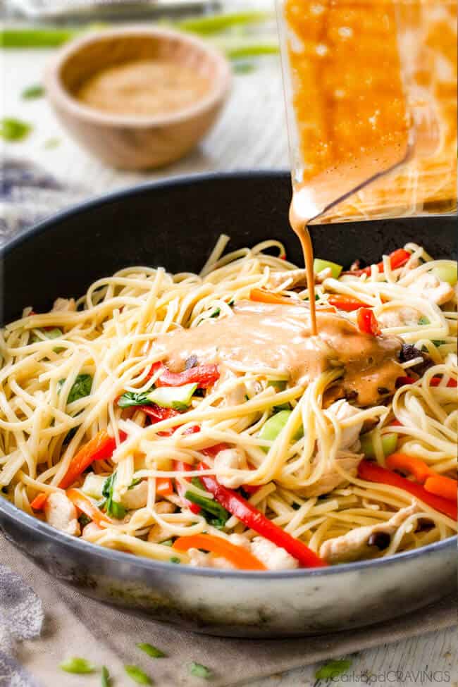 30 Minute Peanut Sesame Noodles (with Chicken and Veggies) - super quick and easy meal all in one with the most amazing creamy peanut sesame sauce you will crave for days! Pouring sesame sauce over noodle and vegetables to make Sesame Noodles