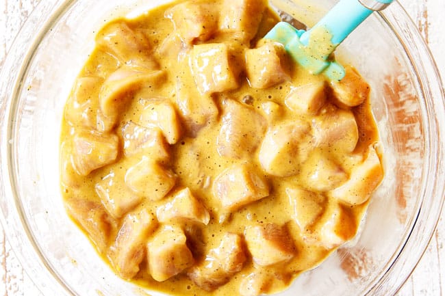 showing how to make lemon chicken by adding chicken to the batter in a glass bowl