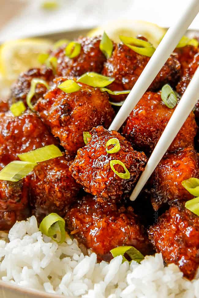 Crispy Chinese Lemon Chicken with green onion on top being picked up with chop sticks.