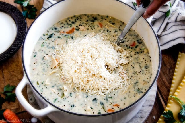 Showing how to make White Chicken Lasagna Soup adding cheese to the pot.