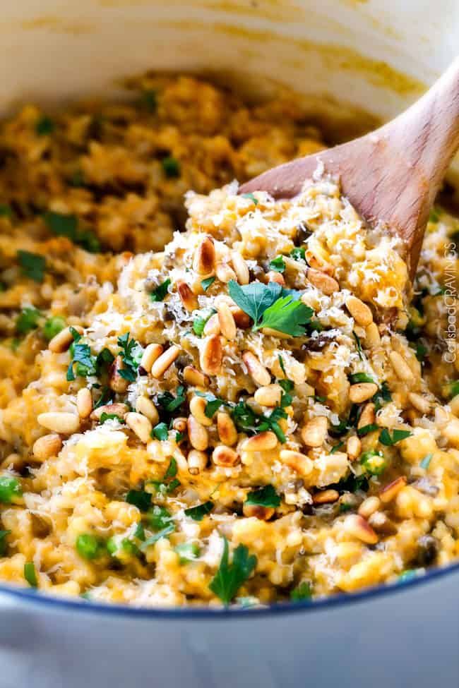 No Babysitting, easy, creamy BAKED Butternut Squash Risotto with Pine Nuts and Pepper Jack! This simple to prepare risotto is wonderfully smooth and creamy, seasoned to perfection and is absolutely fool proof! It makes the most amazing Thanksgiving or holiday side but is easy enough for every day! a wooden spoon stirring best Butternut Squash Risotto in a white pot