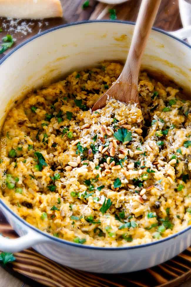 No Babysitting, easy, creamy BAKED Butternut Squash Risotto with Pine Nuts and Pepper Jack! This simple to prepare risotto is wonderfully smooth and creamy, seasoned to perfection and is absolutely fool proof! It makes the most amazing Thanksgiving or holiday side but is easy enough for every day! side shot of baked Butternut Squash Risotto in a white stock pot with a wooden spoon