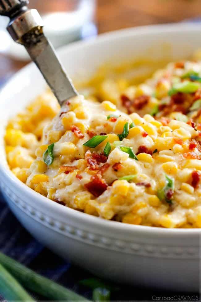 Slow Cooker Creamed Corn with Ricotta and Bacon - this has to be the BEST CREAMED CORN I've eaten in my entire life! Rich and creamy, seasoned to perfection, SO easy and practically fool proof! Definitely making this every Thanksgiving from now on! a servings spoon scooping up easy creamed corn with bacon and green onions in a white bowl