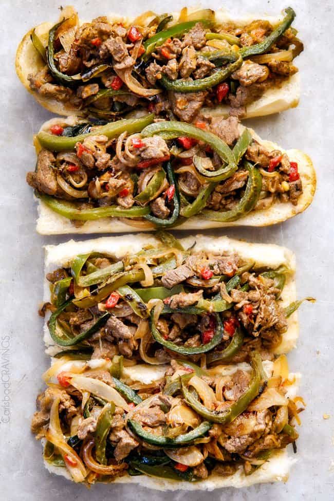 showing how to make Philly Cheesesteak Sandwich recipe by adding the steak, bell peppers and cheese filling on hoagie buns