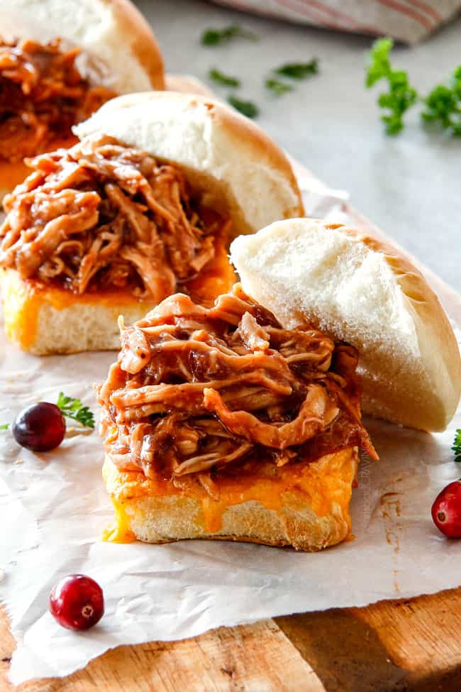 20 Minute Chipotle BBQ Cranberry Turkey Sliders (or chicken!) are a wonderfully delicious way to devour your Thanksgiving turkey leftovers or SO good you will want to make them forever and ever with chicken! And donโt skip the crunchy, sweet and tangy out of this world Apple Poppy Seed Slaw! a row of pulled turkey sliders on a cutting board