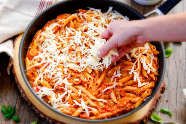 Adding cheese to Cheesy Penne & New York Bakeryยฎ Bake Garlic Bread.