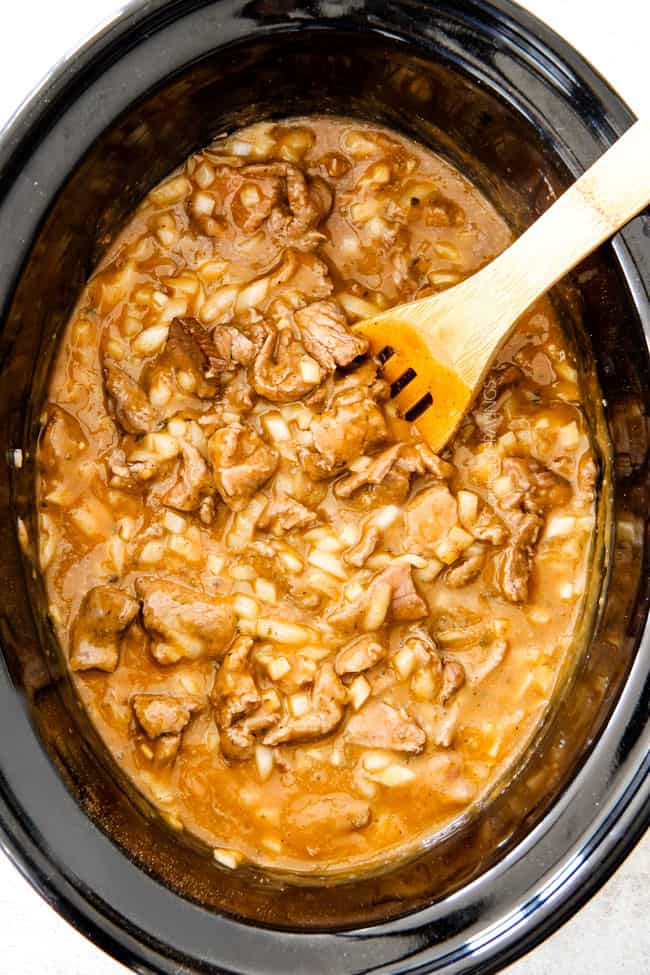 This is by far my family's favorite Slow Cooker Beef Stroganoff recipe! An ultra rich and creamy, amazingly flavorful sauce (without any "cream of" anything!), crazy tender meat all made in the crockpot for a gourmet meal with hardly any effort! I love serving this for holidays like Christmas! showing how to make easy Slow Cooker Beef Stroganoff by stirring together gravy, meat, onions and mushrooms in a black cork pot with a wooden spoon