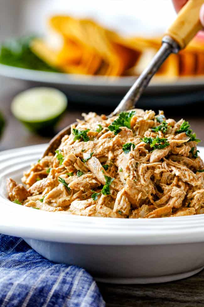 Slow Cooker Fiesta Ranch Cream Cheese Chicken is wonderfully creamy, seasoned to perfection and is as easy as dump and run! It makes the perfect make ahead filling for taquitos, tacos and burritos! slow cooker cream cheese chicken in a white bowl