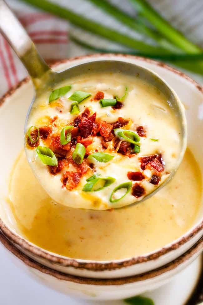 This Skinny Slow Cooker Potato Soup is unbelievably creamy, super flavorful and absolutely the best I've ever tried! and its super easy in the crock pot! holding up a ladle of cream crockpot potato soup with bacon and green onions