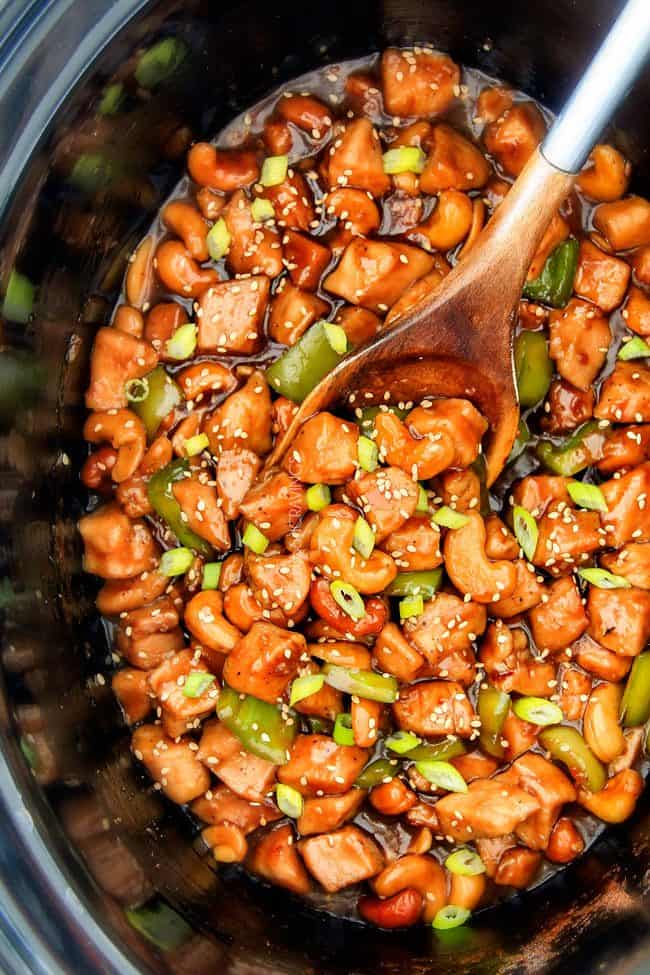 Slow Cooker Chinese Cashew Chicken- this is the best cashew chicken I have ever tried! the chicken is incredibly tender, the sauce is wonderfully flavorful and the punch of buttery, creamy cashews is out of this world! Definitely a family favorite and so much heather than takeout! top view of easy Crock Pot Cashew Chicken in the slow cooker with a wooden spoon