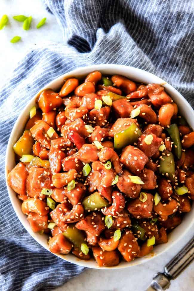 Slow Cooker Chinese Cashew Chicken- this is the best cashew chicken I have ever tried! the chicken is incredibly tender, the sauce is wonderfully flavorful and the punch of buttery, creamy cashews is out of this world! Definitely a family favorite and so much heather than takeout! Top view of Crockpot Cashew Chicken garnished with sesame seeds in a white bowl
