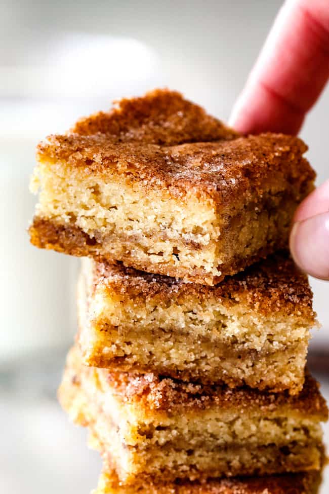 Incredibly EASY, thick, soft and chewy, buttery Snickerdoodle Cookie Bars taste just like the cookie but so much easier and less time consuming! The cinnamon and sugar crackle top is to die for! a hand picking up thick Snickerdoodle Bars